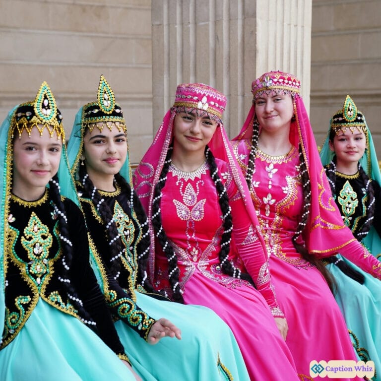 Five women in colorful traditional dresses pose together, adorned with intricate jewelry and headpieces.